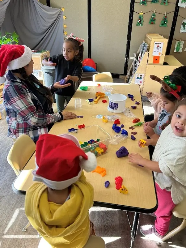A group of children sitting at a table with christmas hats on.