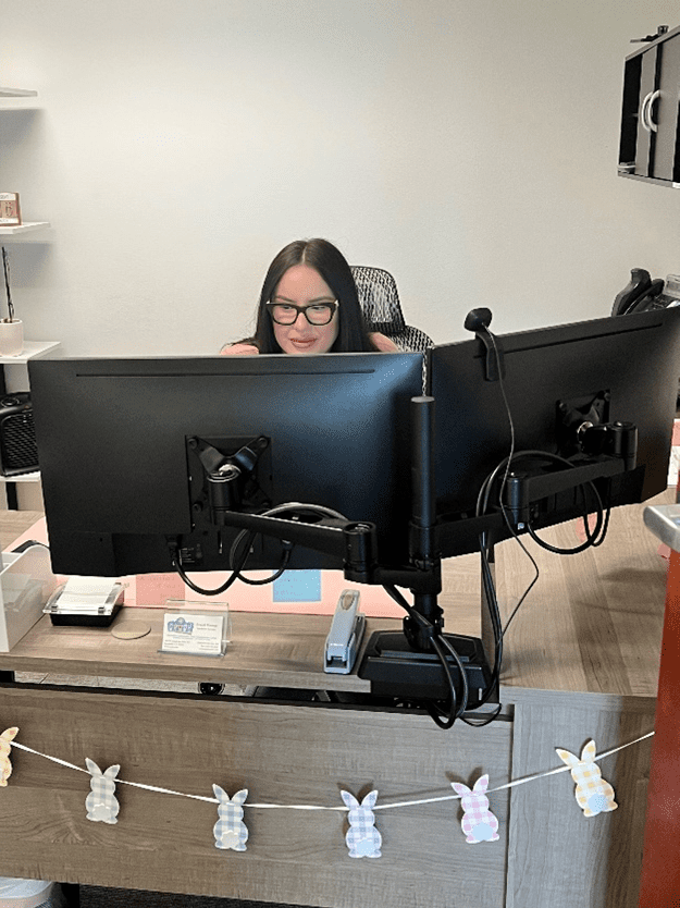 A woman sitting at her desk with two monitors.