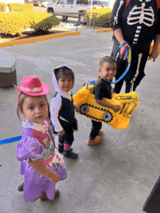 Three children in costumes are standing on the sidewalk.