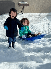 Two children are playing in the snow together.
