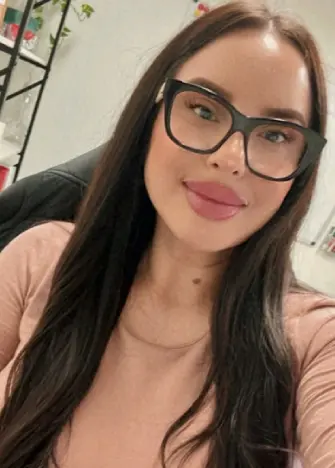 A woman with glasses and long hair wearing a pink shirt.