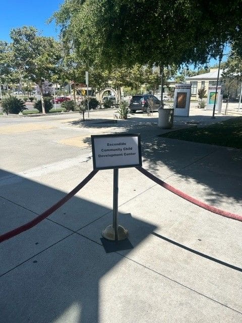 A sign on the sidewalk with red ropes around it.