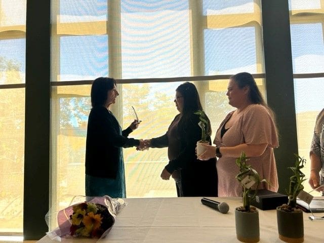 Three women shaking hands in front of a window.